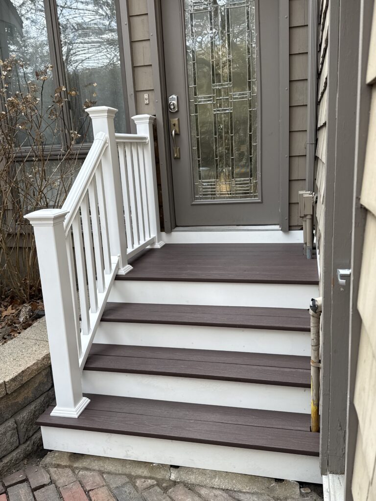 A small set of white wooden stairs leading to a gray door with glass panels.