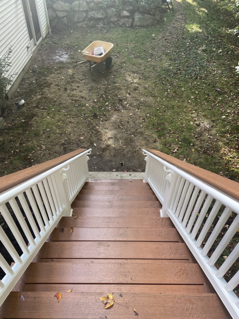A view down wooden stairs to a muddy yard with a small box on the grass.